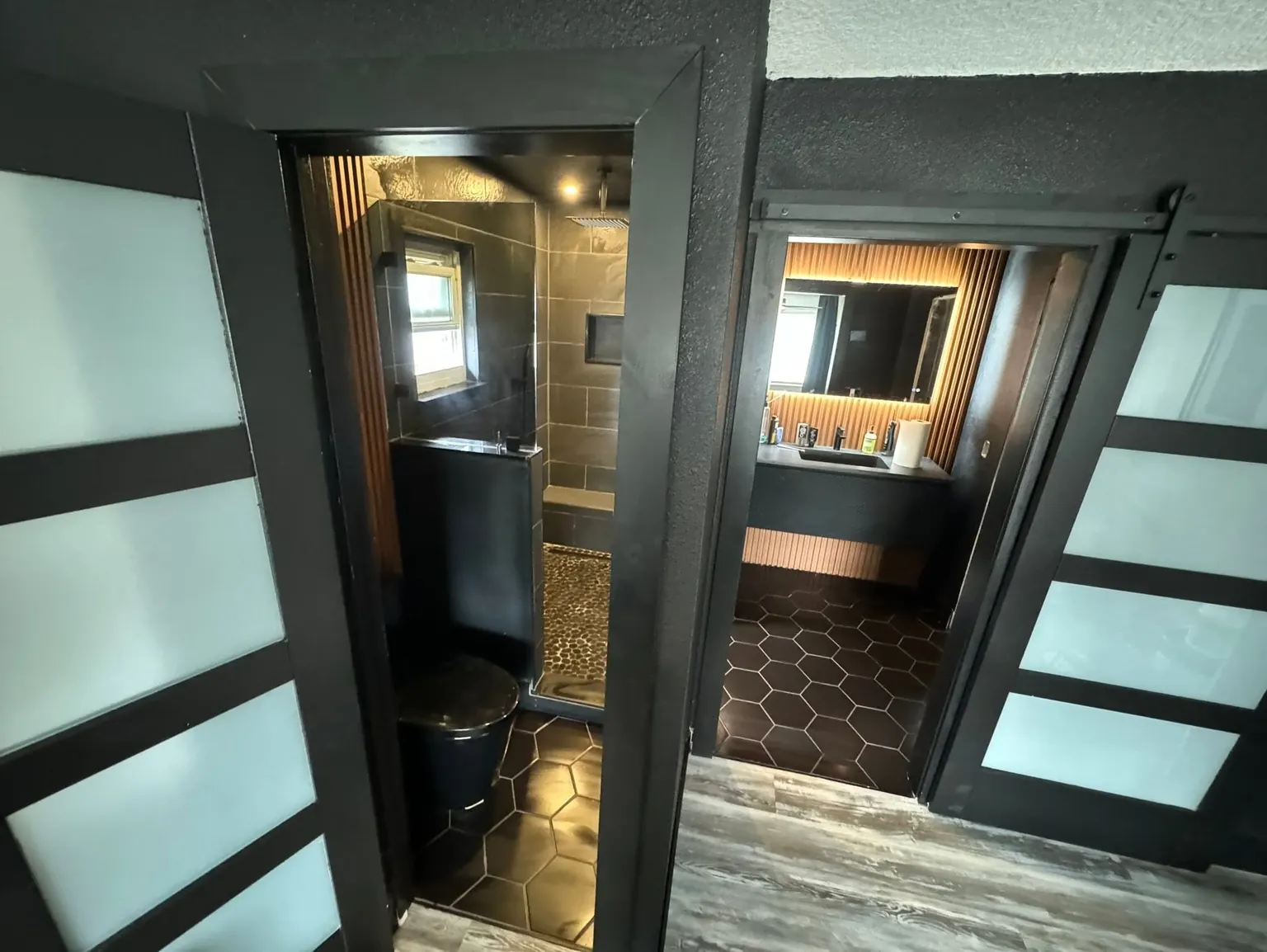 A finished bathroom with black tile, a dark hexagon floor, a walk-in shower and sliding frosted-glass doors.
